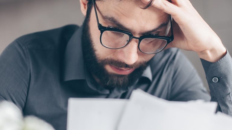 A man looking at a piece of paper with a concerned facial expression and hand on his head. More than 30 per cent of couple households with one full-time earner are in poverty, nearly as high as the rate of hardship for families without any full-time workers