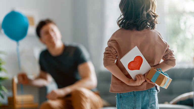 A child approaches a blurred-out fatherlike figure with a card and gift