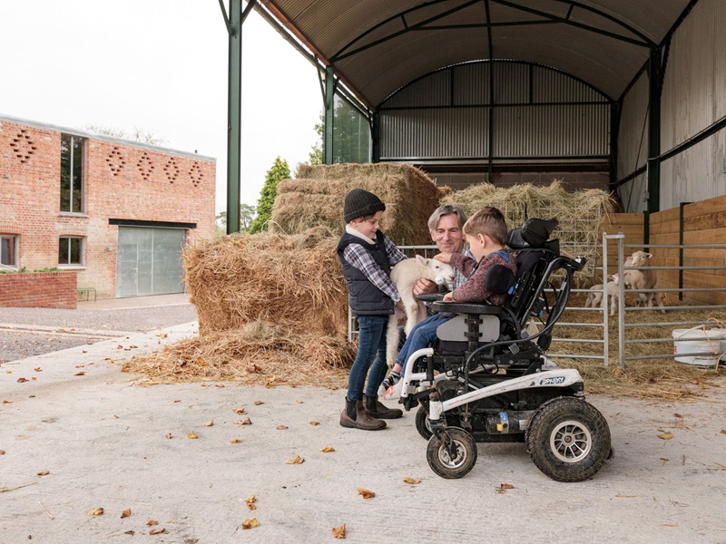 A child and an adult in a  wheelchair play with a farmyard animal at Wraxall Yard