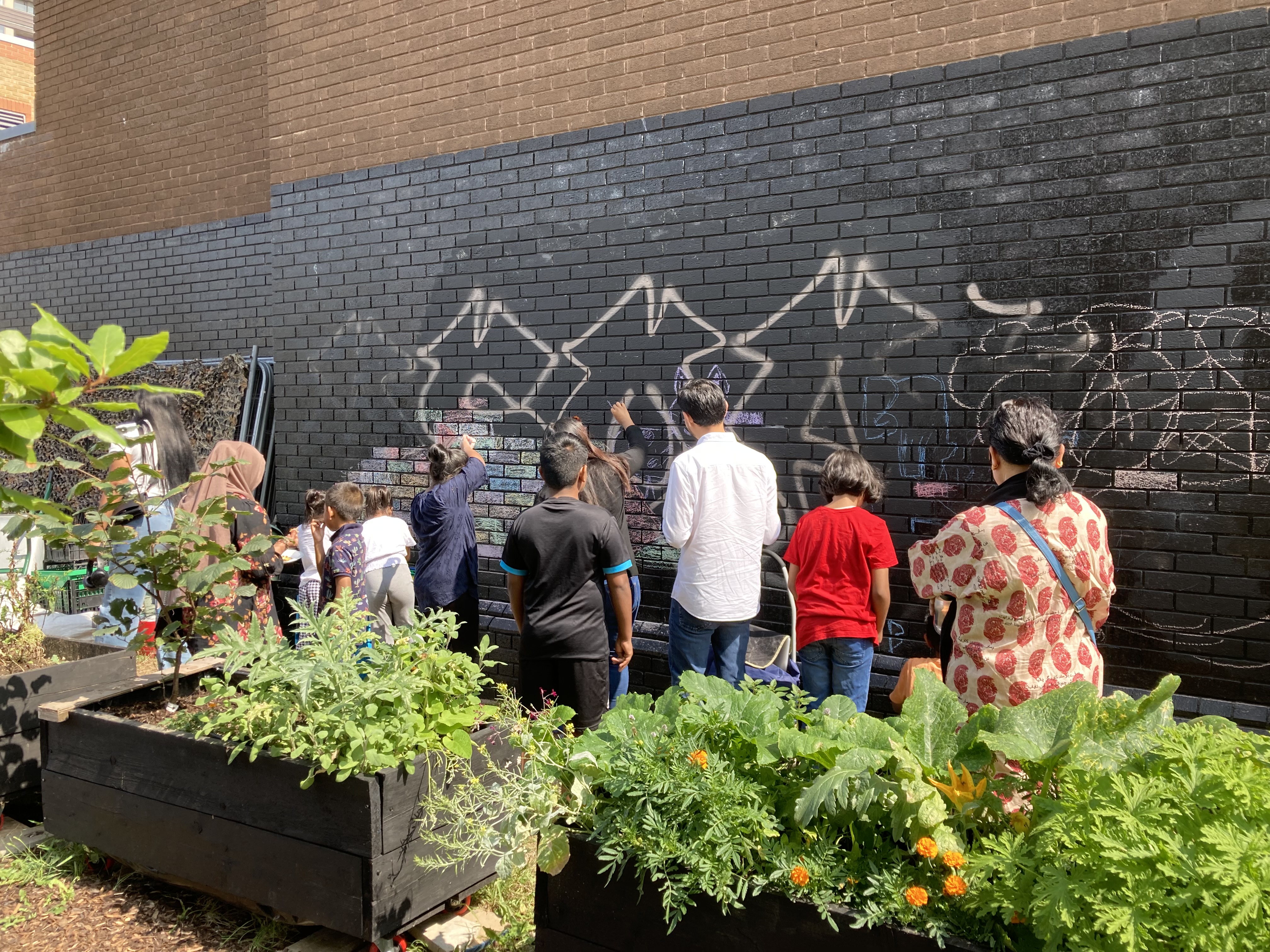 volunteers paint on a black wall in an urban garden in Shadwell, east London