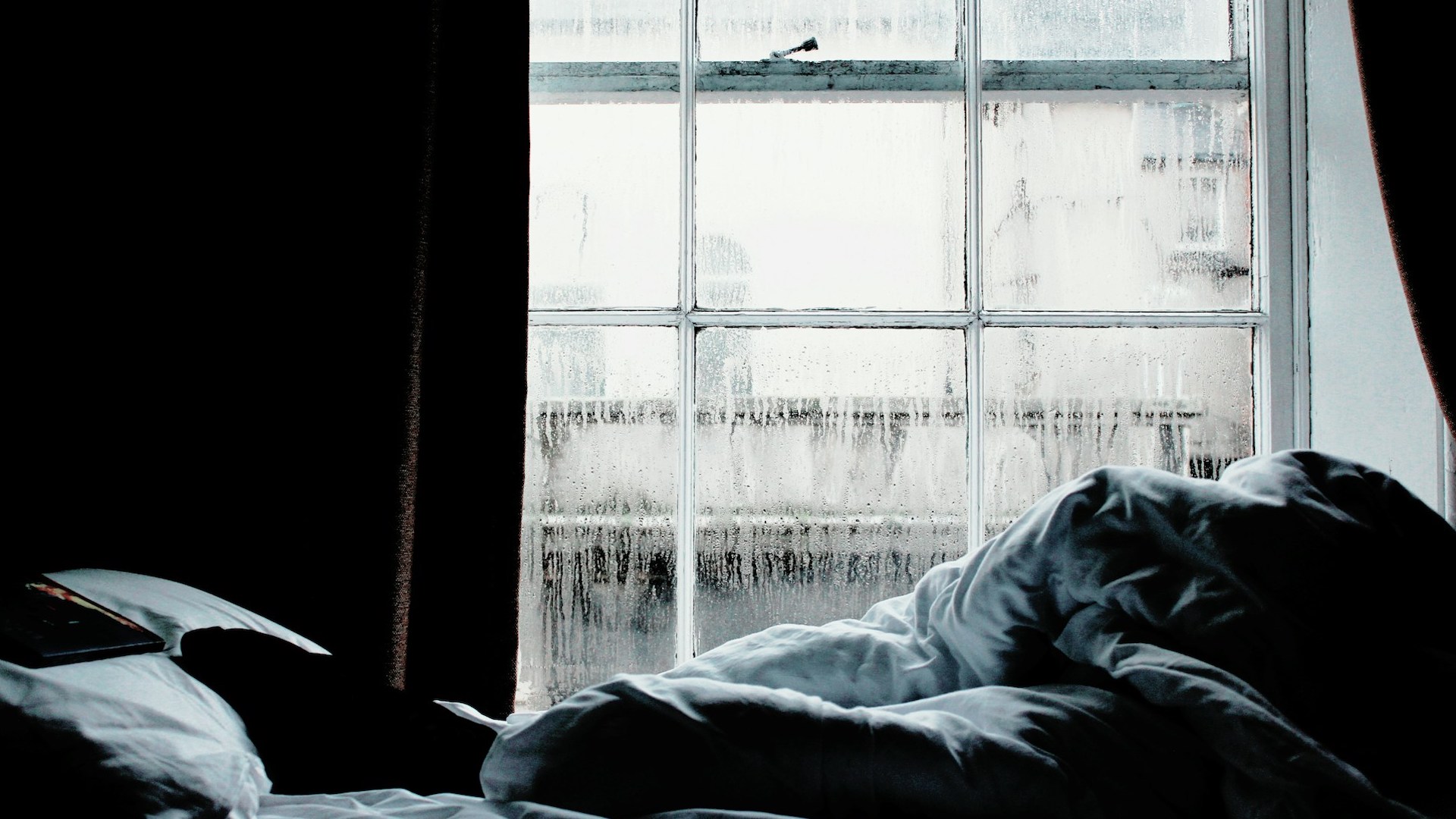 A condensation-covered window behind an unmade bed