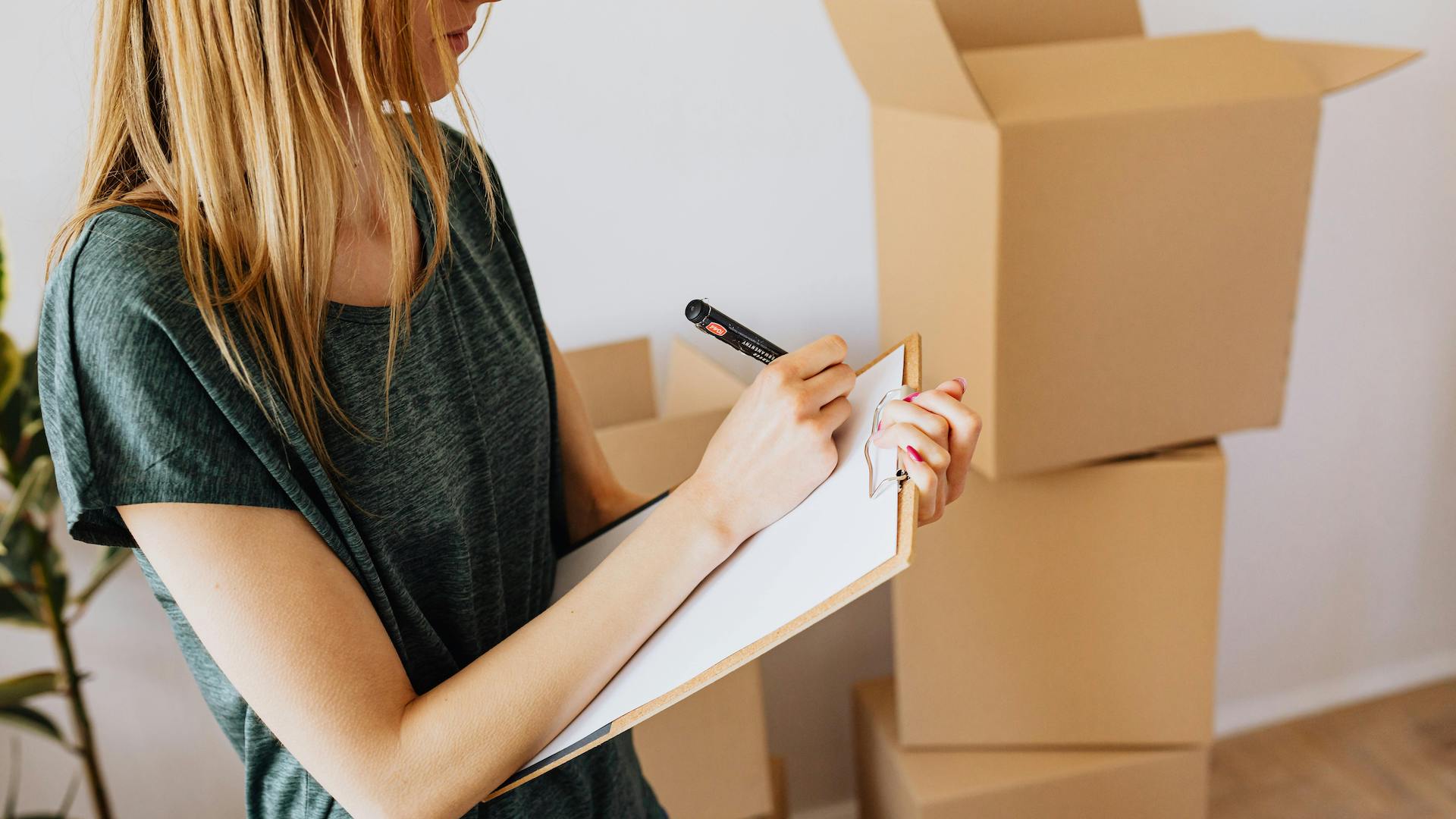 A woman writing on paper with moving boxes stacked behind her