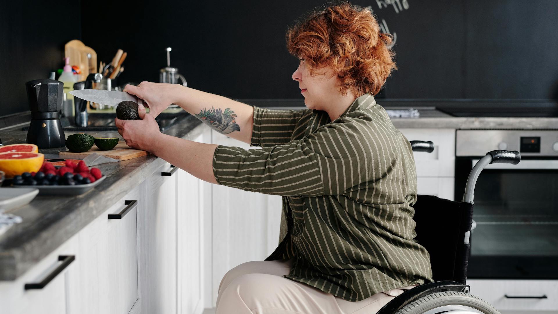 A woman in a wheelchair cutting food on a kitchen counter