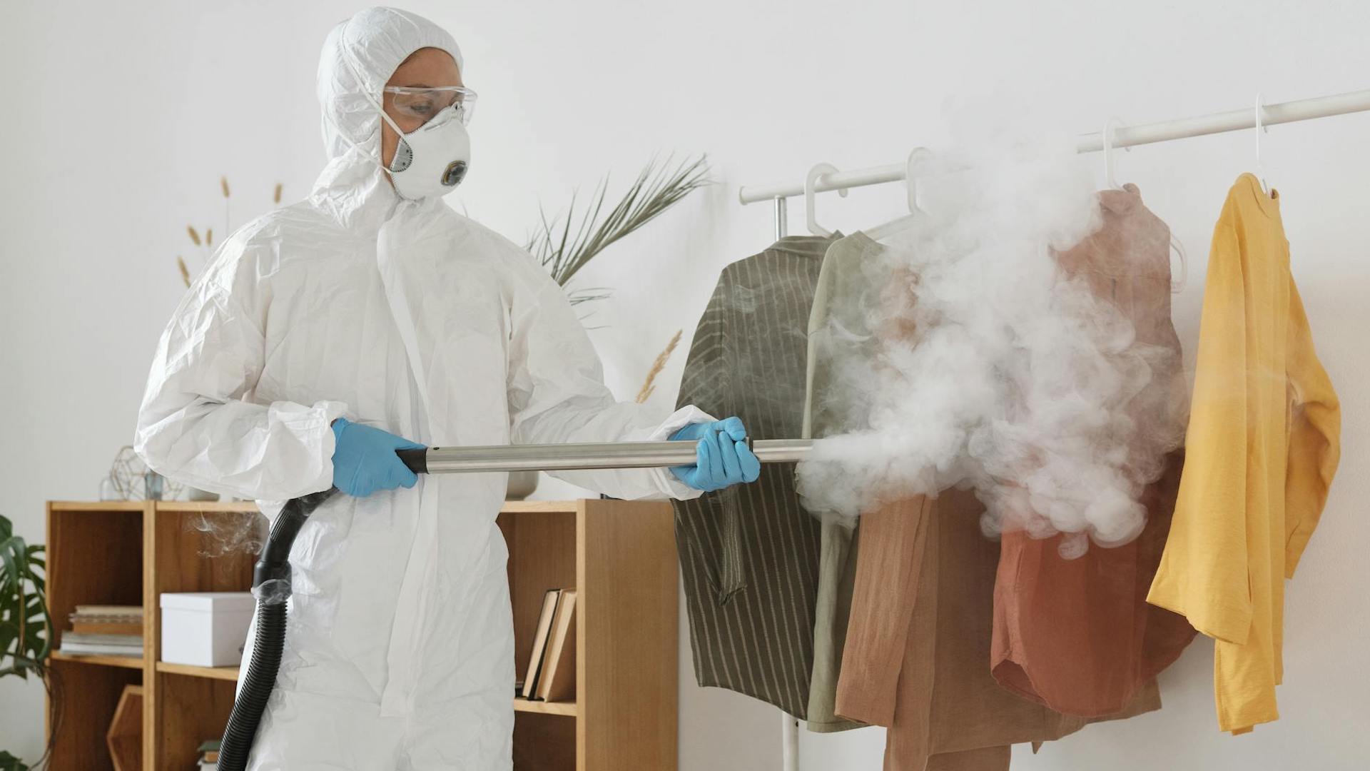 a pest control worker fumigating clothes on a rail