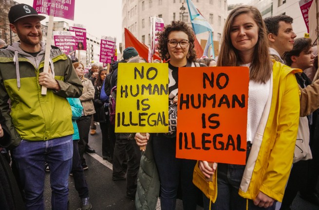 protesters hold two slogans saying 'no human is illegal'