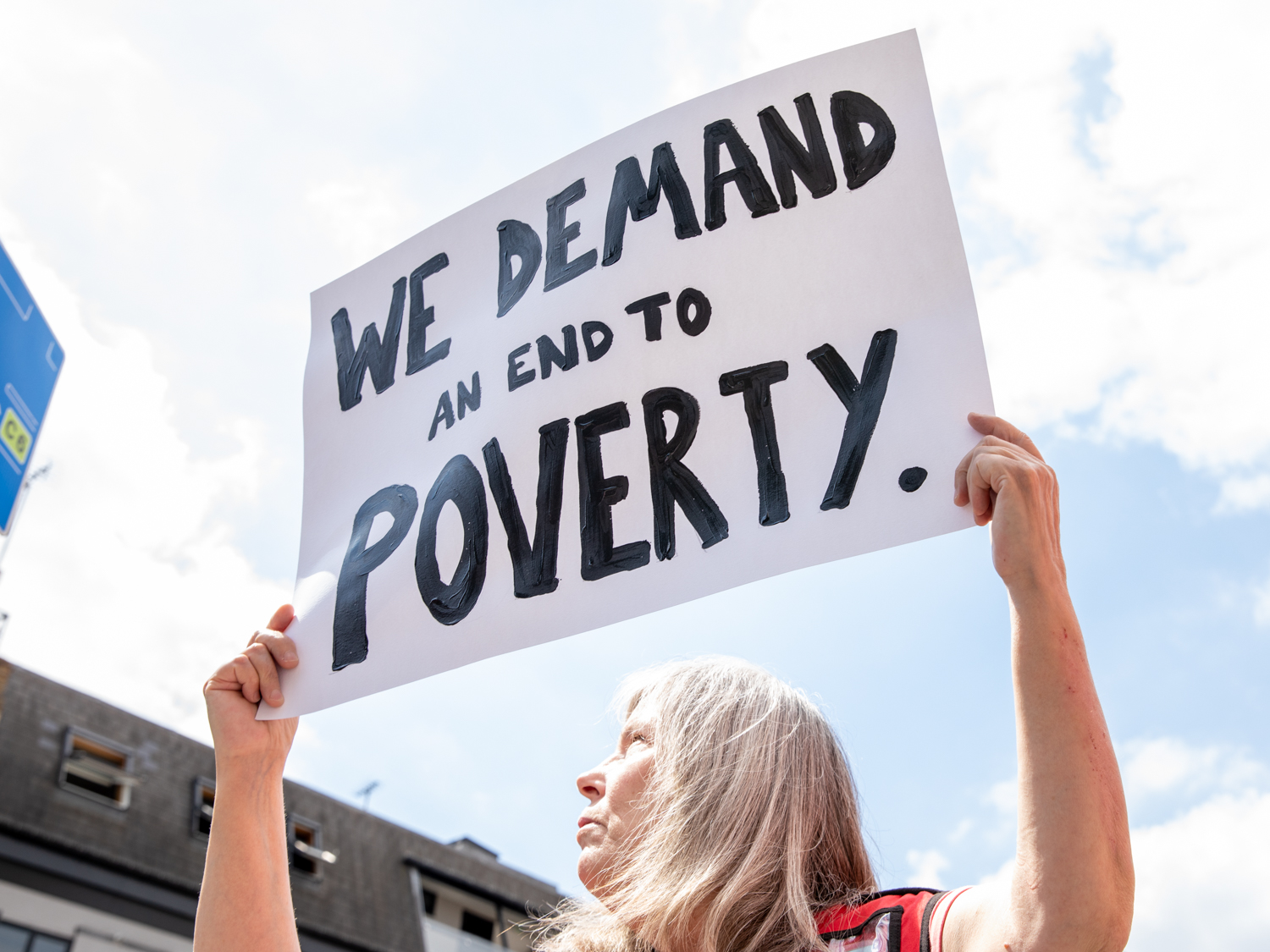 Big Issue vendor holds sign that reads we demand an end to poverty