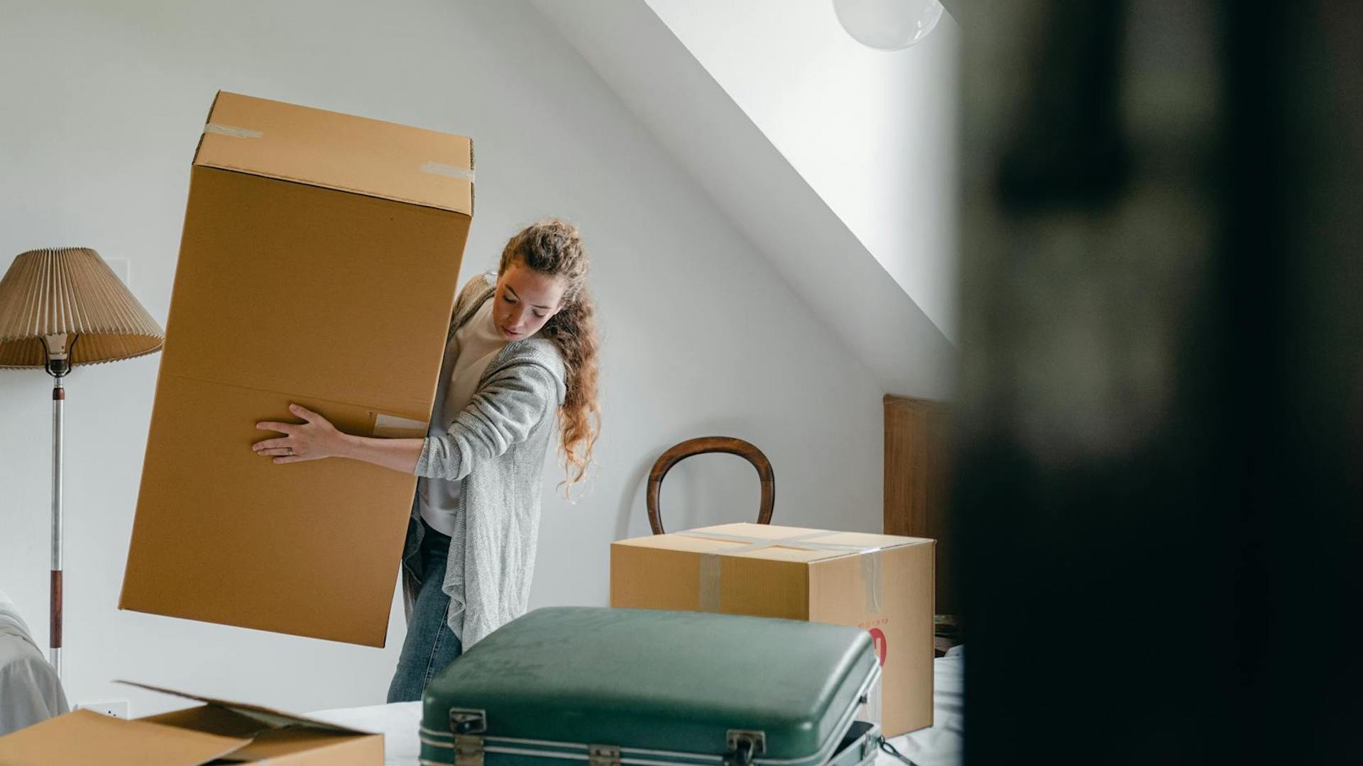 a woman surrounded by moving boxes carrying a larger box