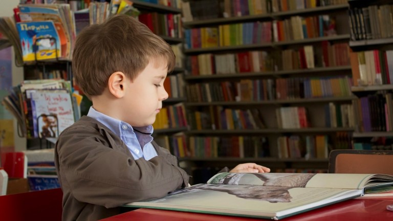 a boy in school uniform reading a book in a school library // special educational needs