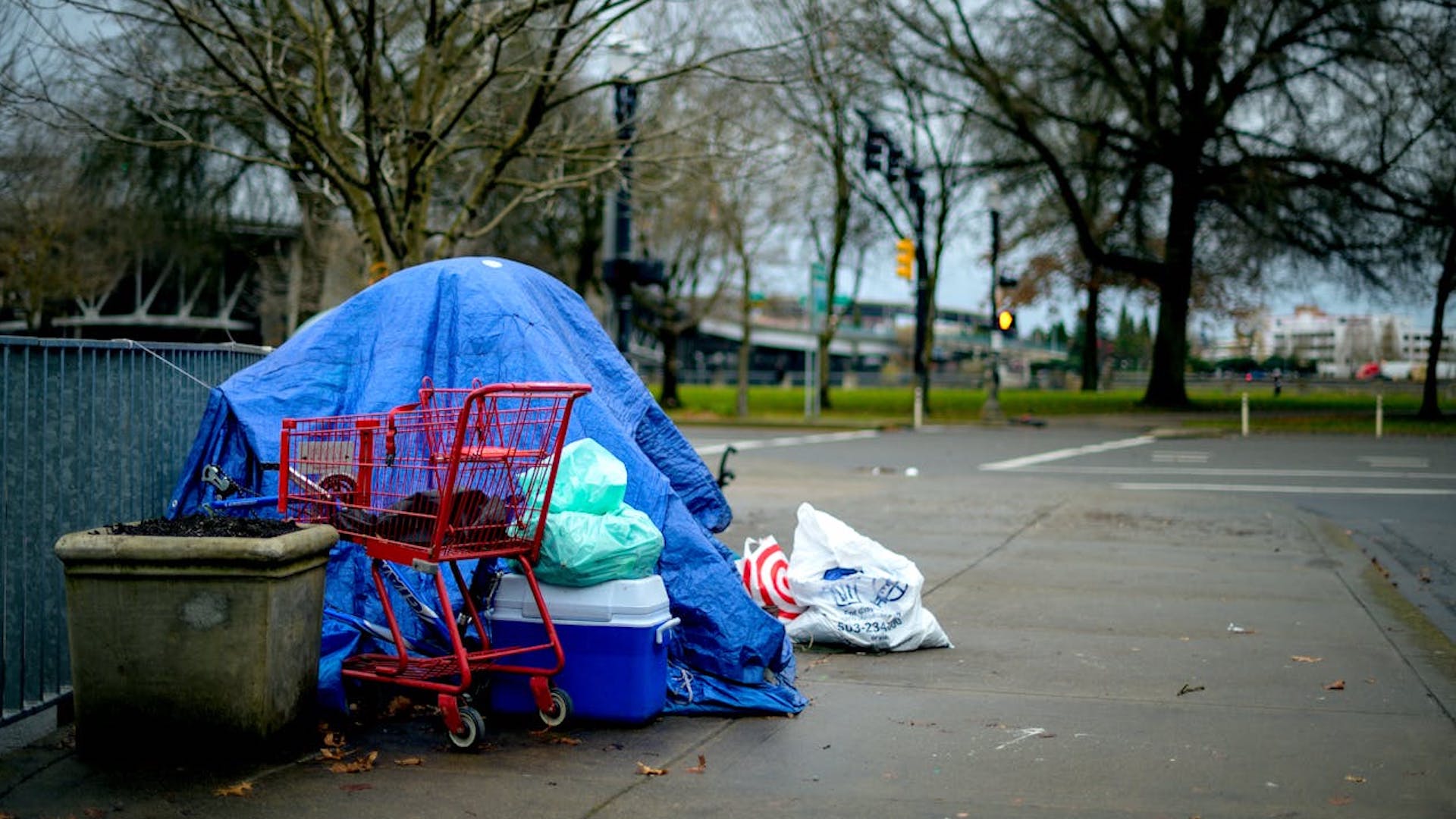 a blue tent pitched in a car park with a shopping trolley and plastic bags leaning against it