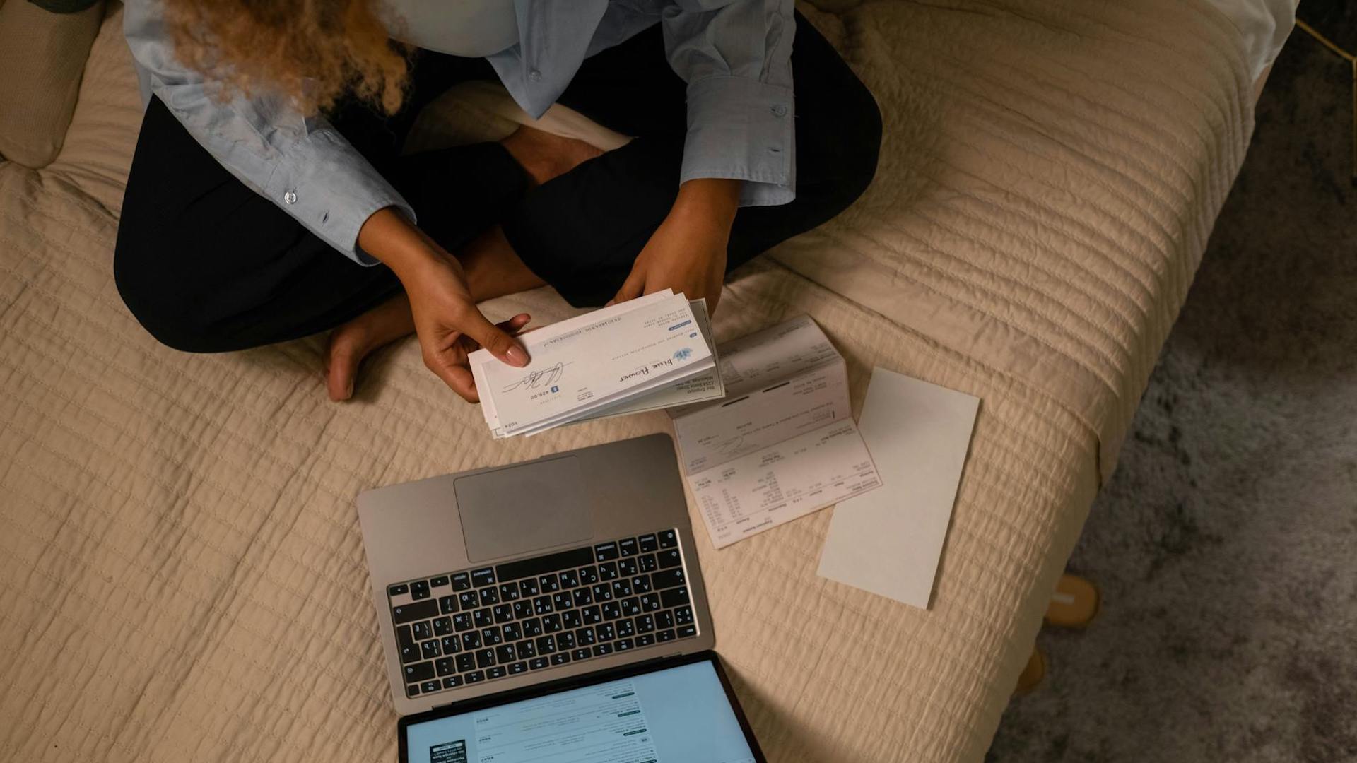 a birds-eye view of someone sitting cross legged on a bed looking at bills // apply for a budgeting loan