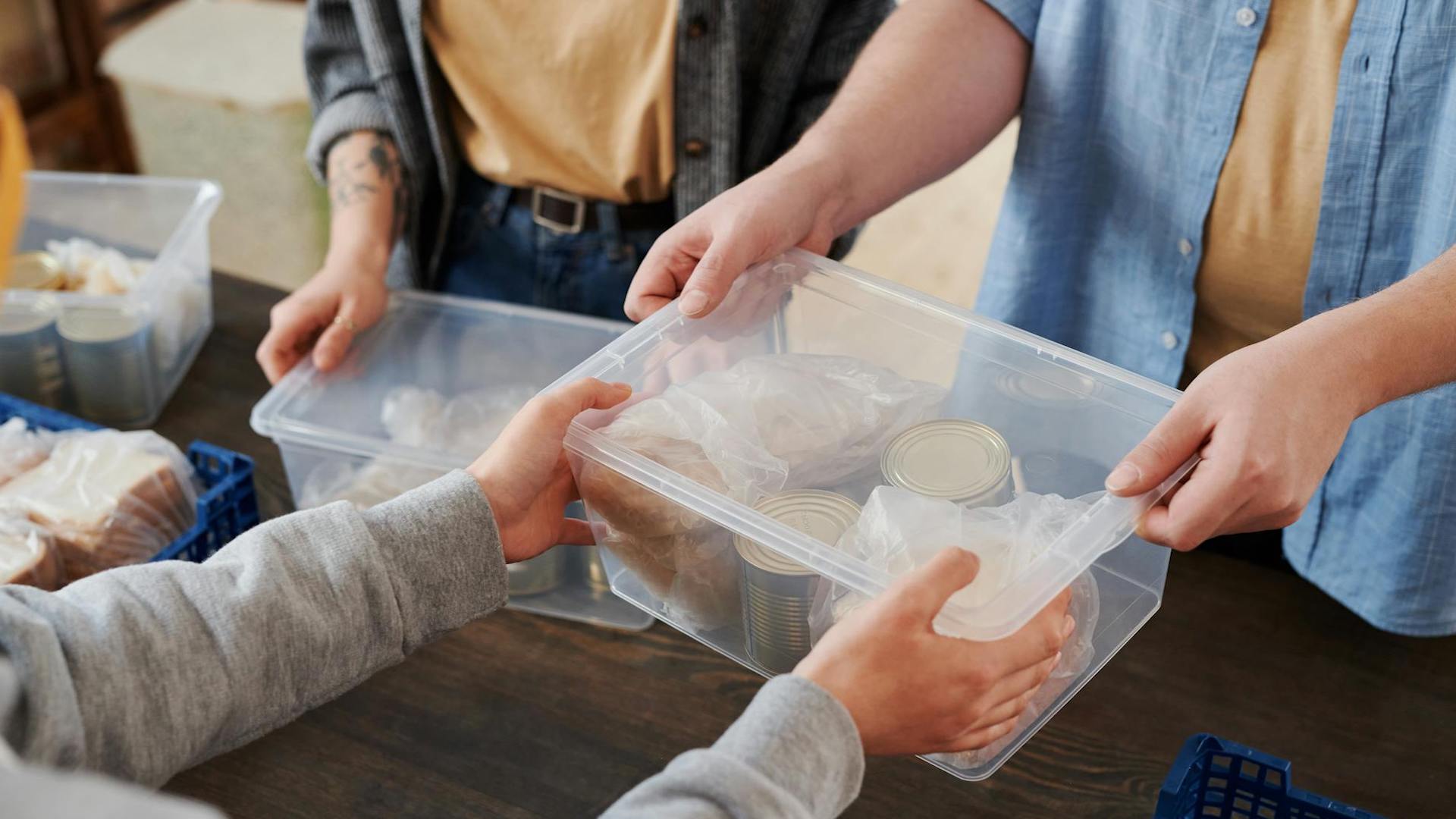 A plastic tubbed filled with food donations being passed across a table between people