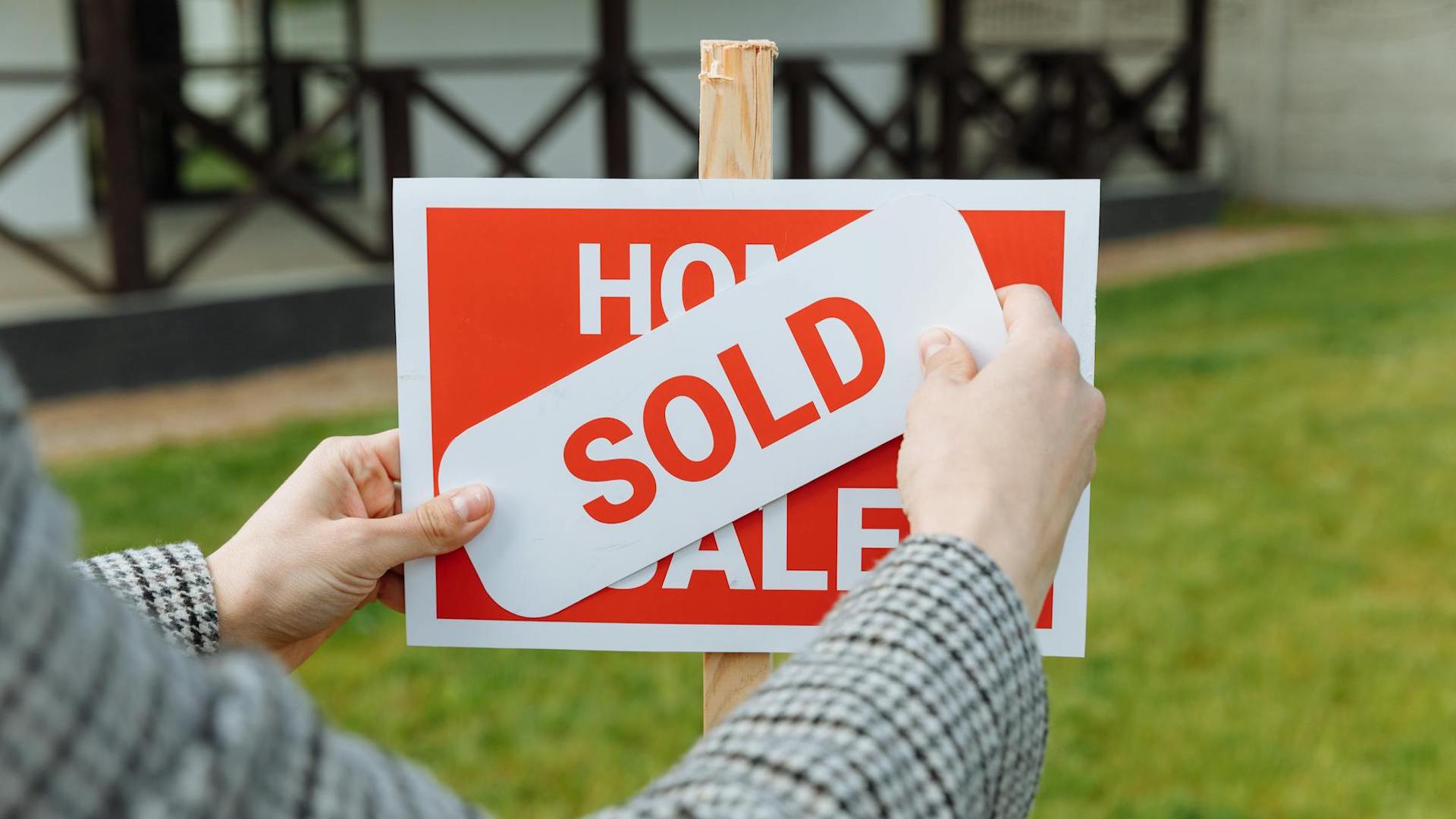 a person's hands are seen pasting a 'sold' sticker over a 'for sale' sign outside a house