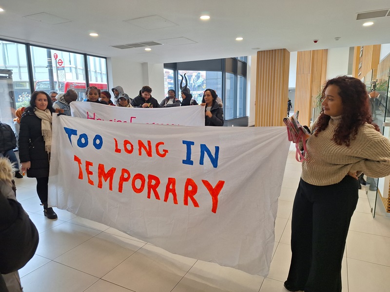 protesters hold a banner reading "Too long in temporary"