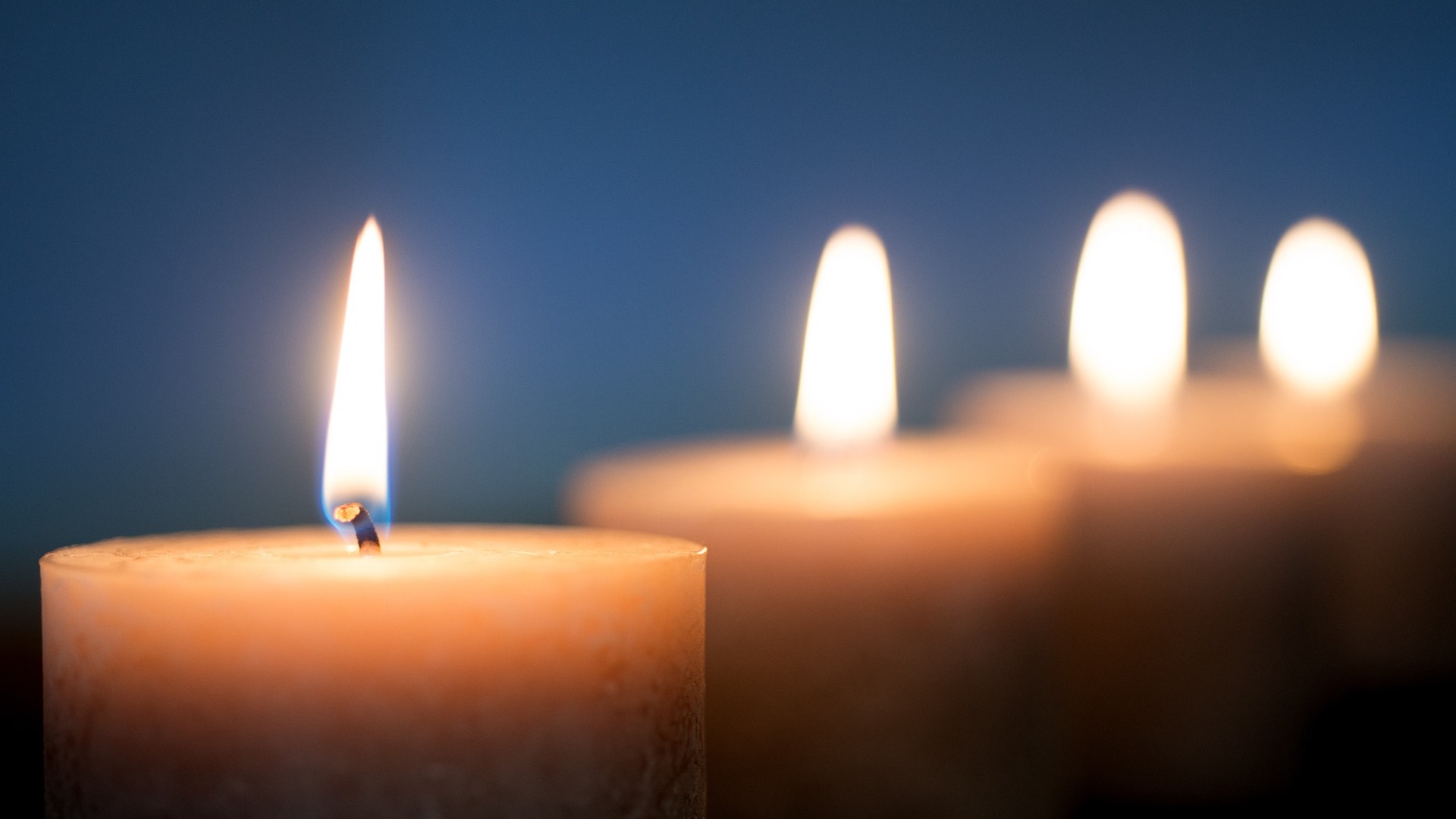 a close-up view of four lit pillar candles against a dark blue background