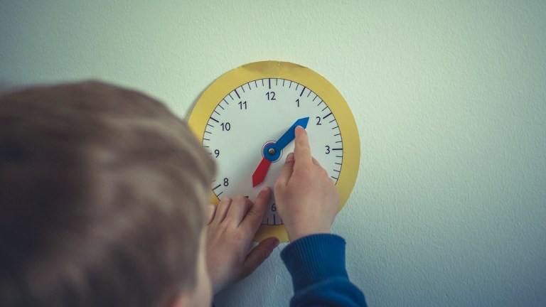 a view of the back of a toddler's head while they play with a paper clock stuck to a white wall