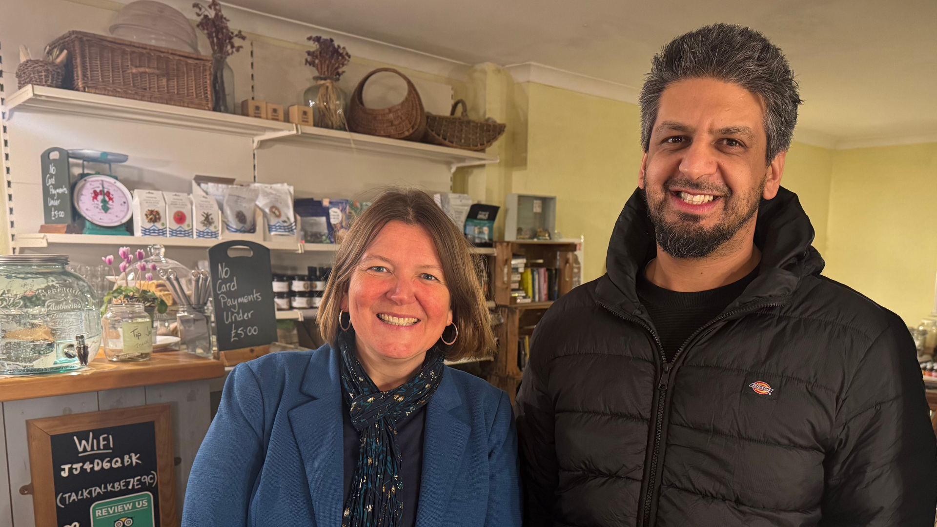 MP Ellie Chowns and Big Issue support worker Mo Afzal smile at the camera, in a cafe in Ledbury, England.