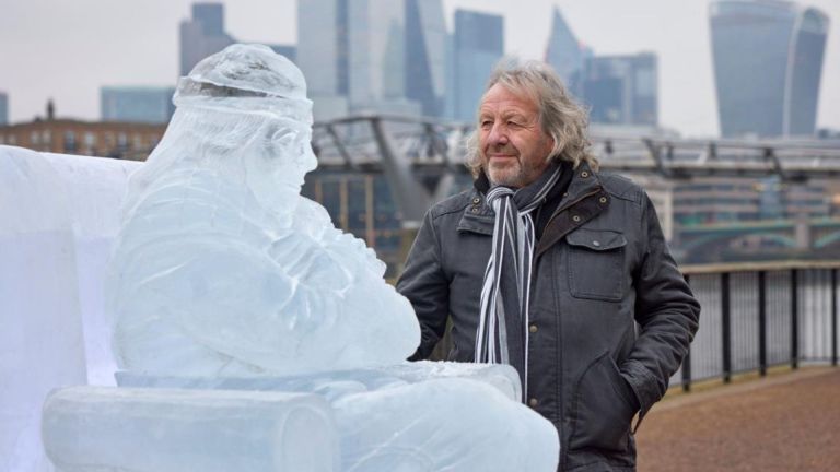 Pensioner Rob Trewhella stands next to an ice sculpture in his image as a protest to cuts to winter fuel payments