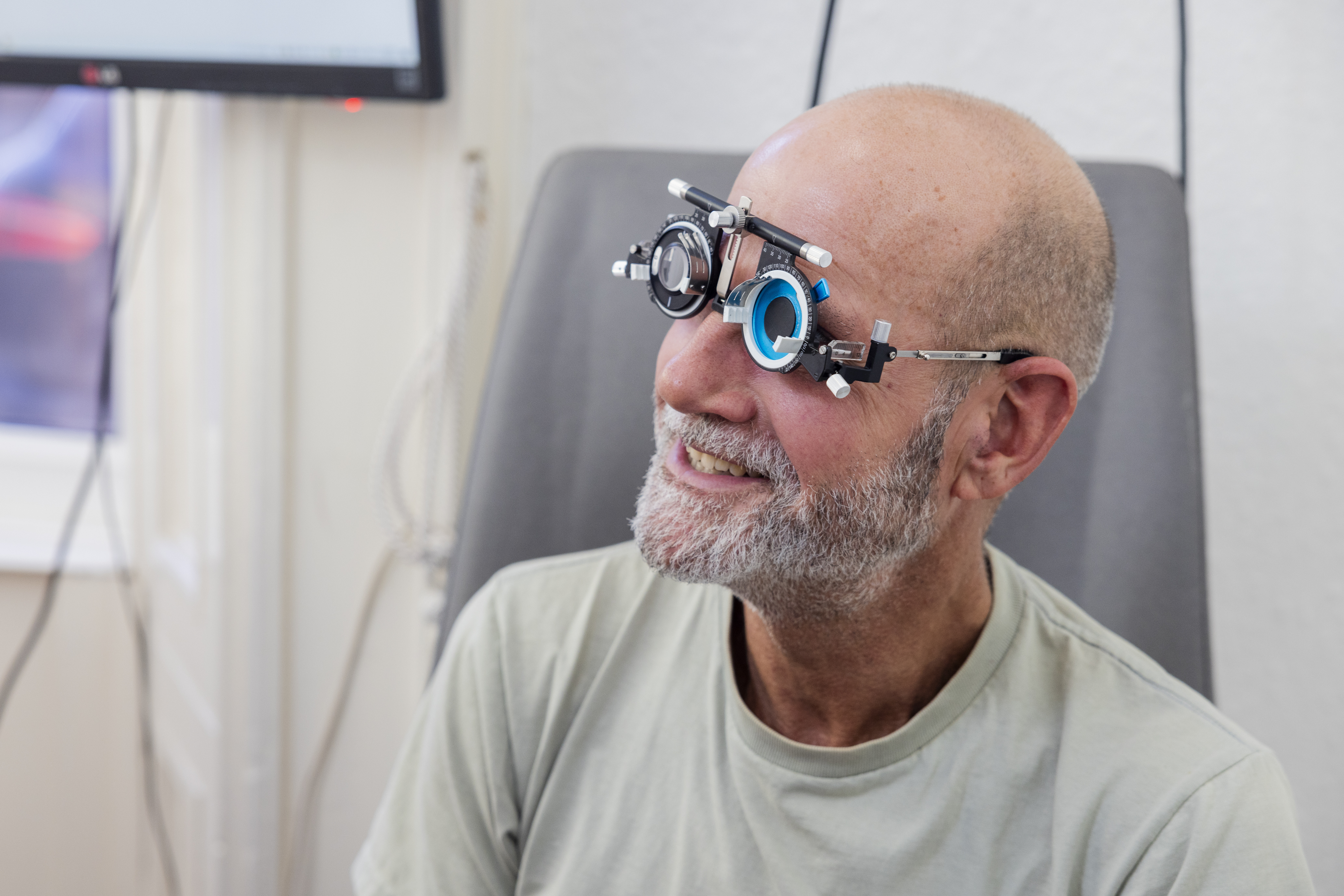 A man smiles while wearing trial lenses during an eye examination, with an optometry trial lens frame fitted on his face.