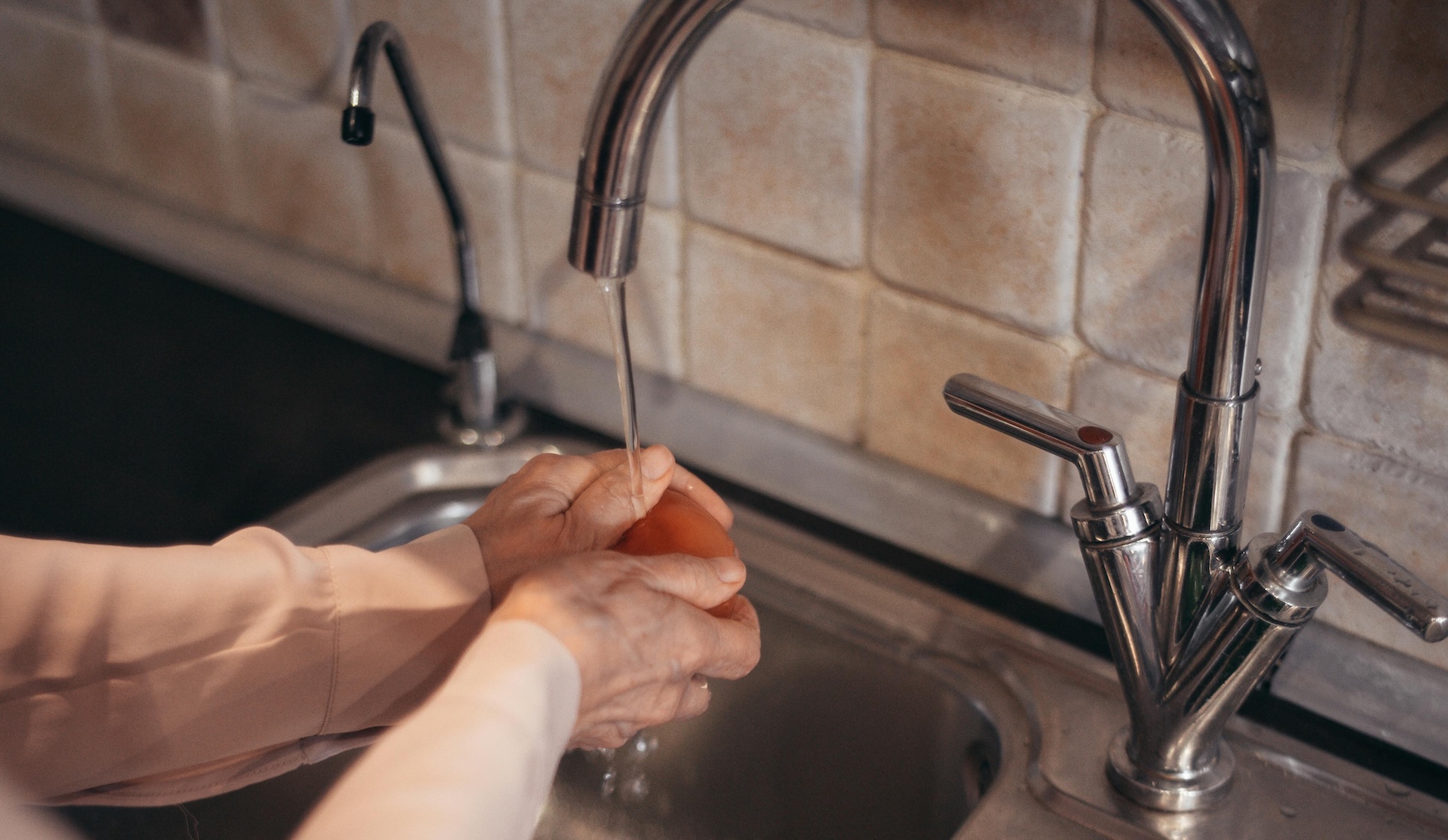 elderly woman washing food in tap water